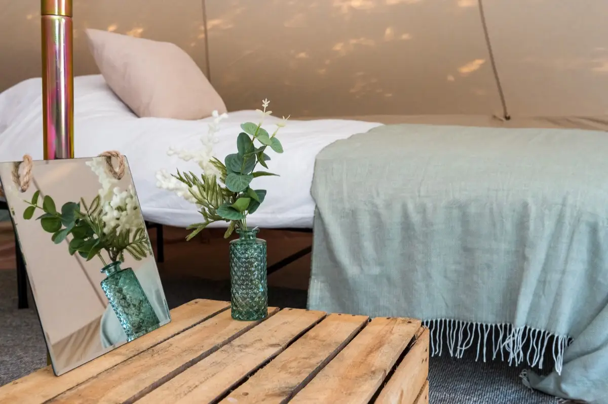 A made-up bed and a crate side table inside a bell tent